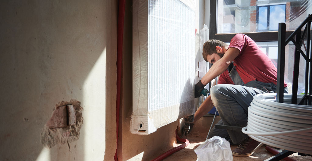 Two craftsmen working together on an installation in a basement undergoing finishing, seen from behind, focused on their task